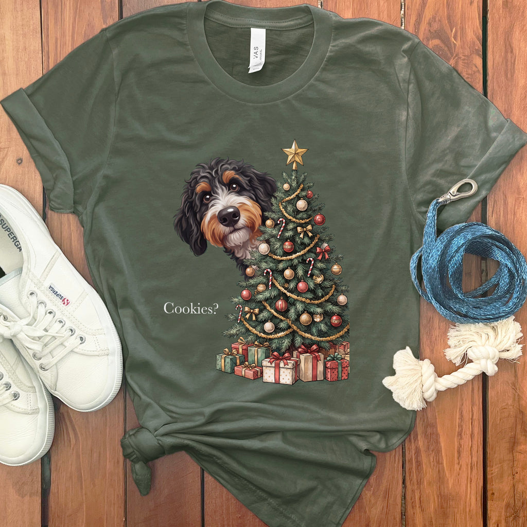 Bernedoodle peeking from behind a decorated Christmas tree with presents below, text "Cookies?"
