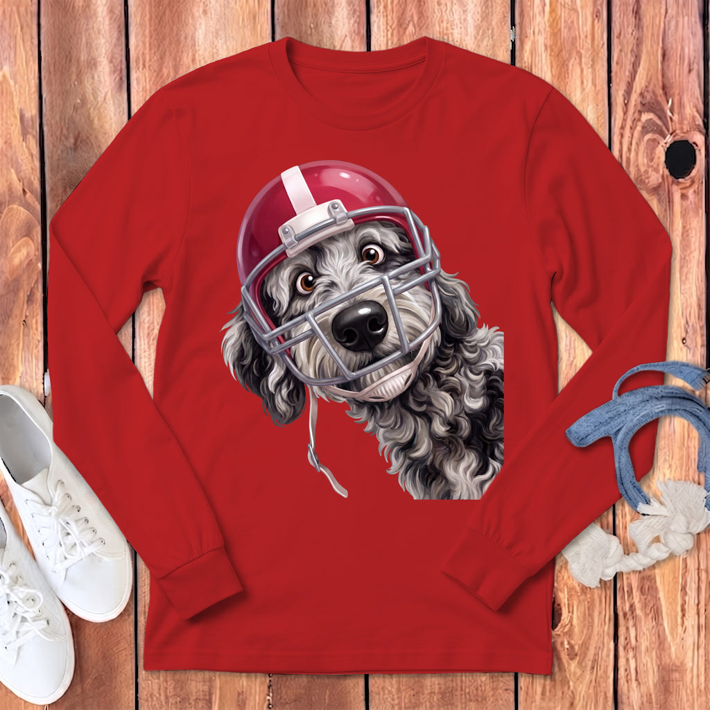 Black and white curly dog wearing a red football helmet on a red long-sleeve shirt.