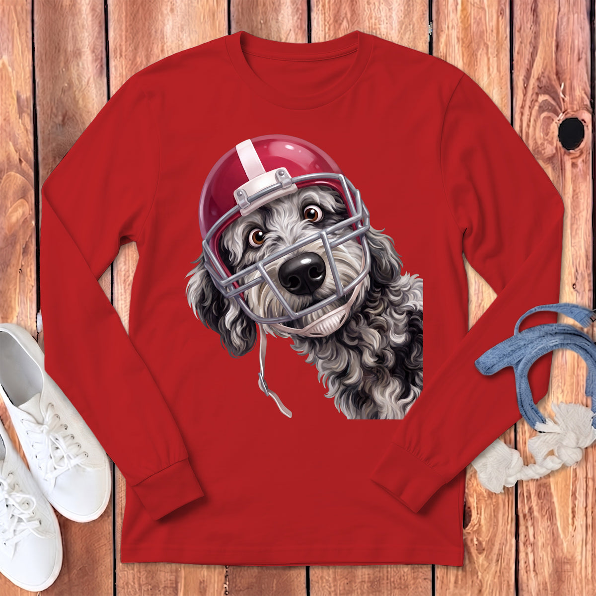 Black and white curly dog wearing a red football helmet on a red long-sleeve shirt.