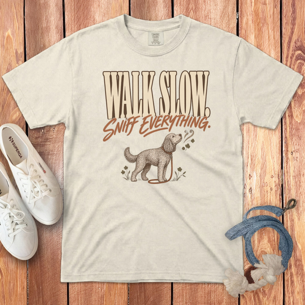 A cream-colored t-shirt with the brown text Walk Slow Sniff Everything and an illustration of a dog.