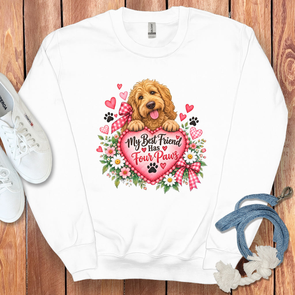 White crewneck sweatshirt featuring a graphic of a fluffy dog resting on a pink heart surrounded by flowers, hearts, and paw prints, with the text My Best Friend Has Four Paws.