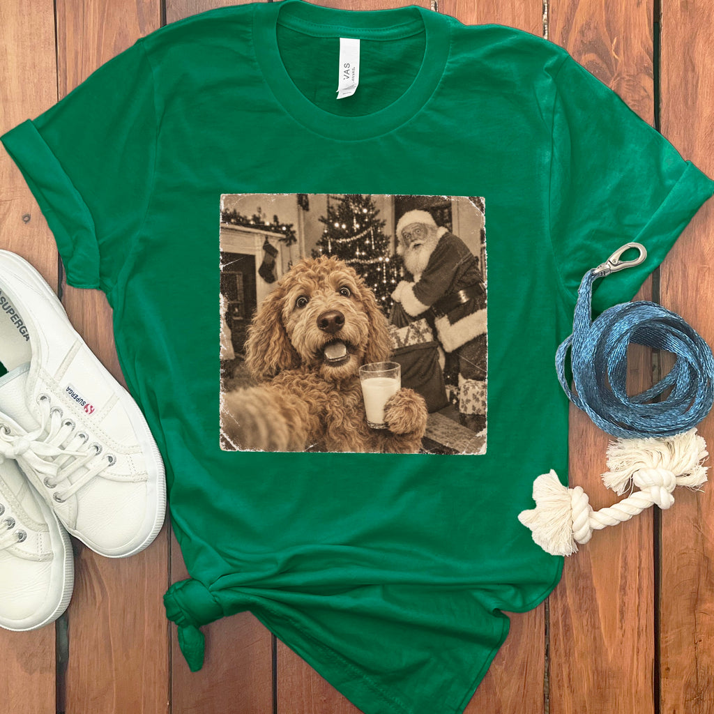 A green t-shirt with a vintage-style graphic of a doodle dog holding a glass of milk in front of Santa.
