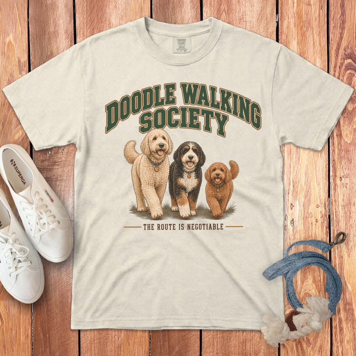 Off-white t-shirt with Doodle Walking Society graphic, three dogs, and white sneakers on wooden background.