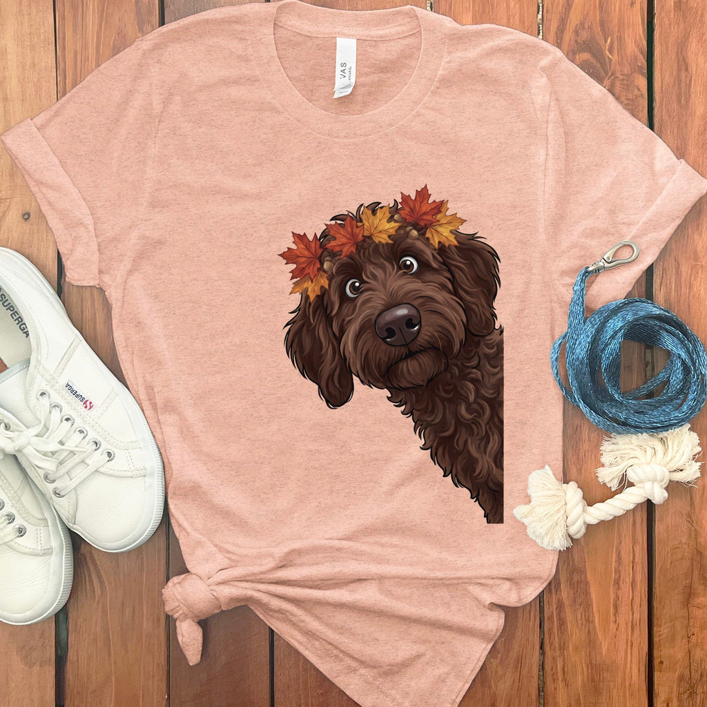 Brown dog with autumn leaves crown on peach t-shirt, next to white sneakers.