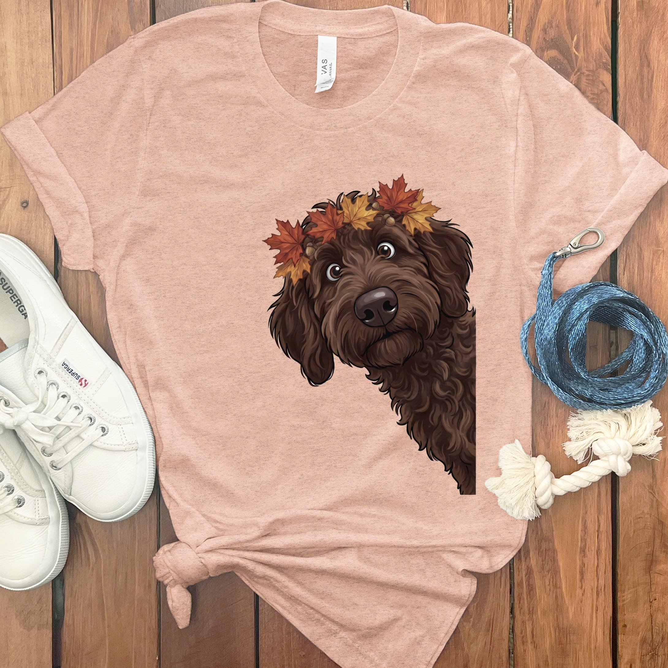 Brown dog with autumn leaves crown on peach t-shirt, next to white sneakers.