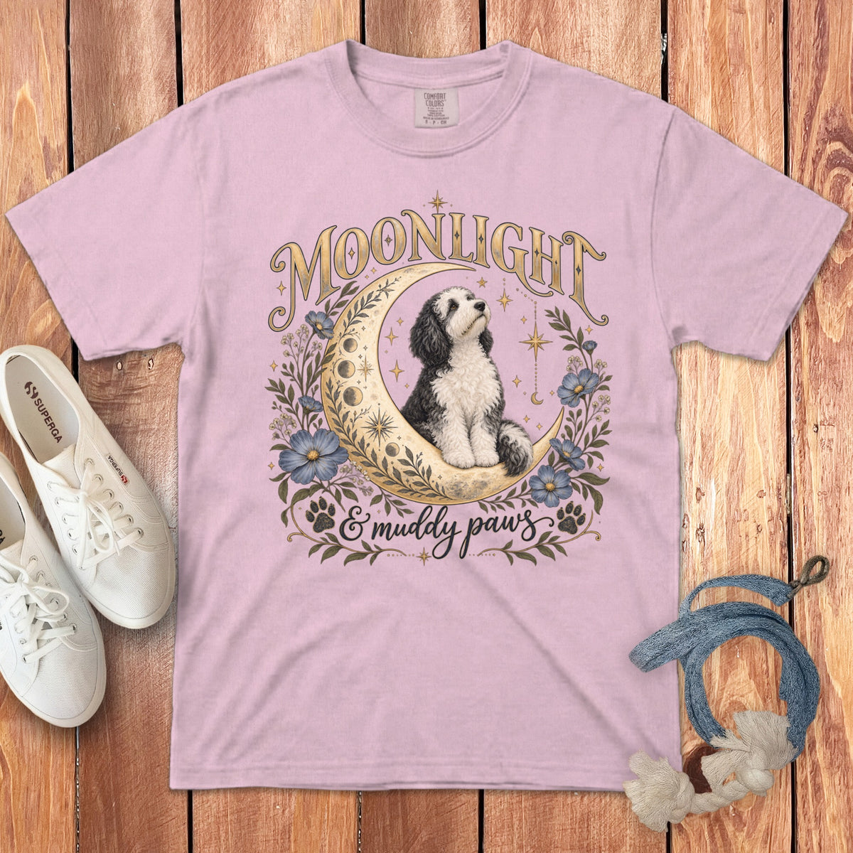 Pink t-shirt with a graphic of a dog on a crescent moon surrounded by flowers, text, and paw prints.