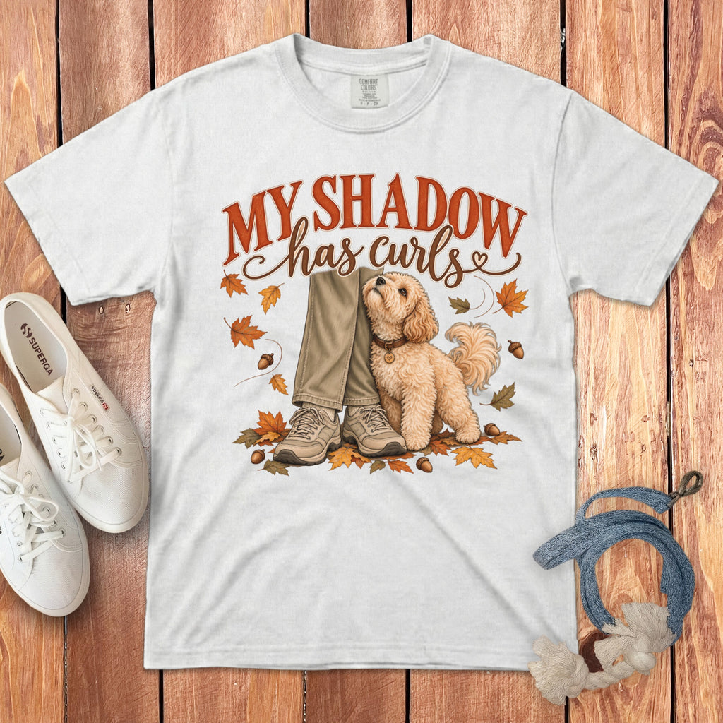 White t-shirt with a graphic of a fluffy dog sitting beside legs, surrounded by autumn leaves.