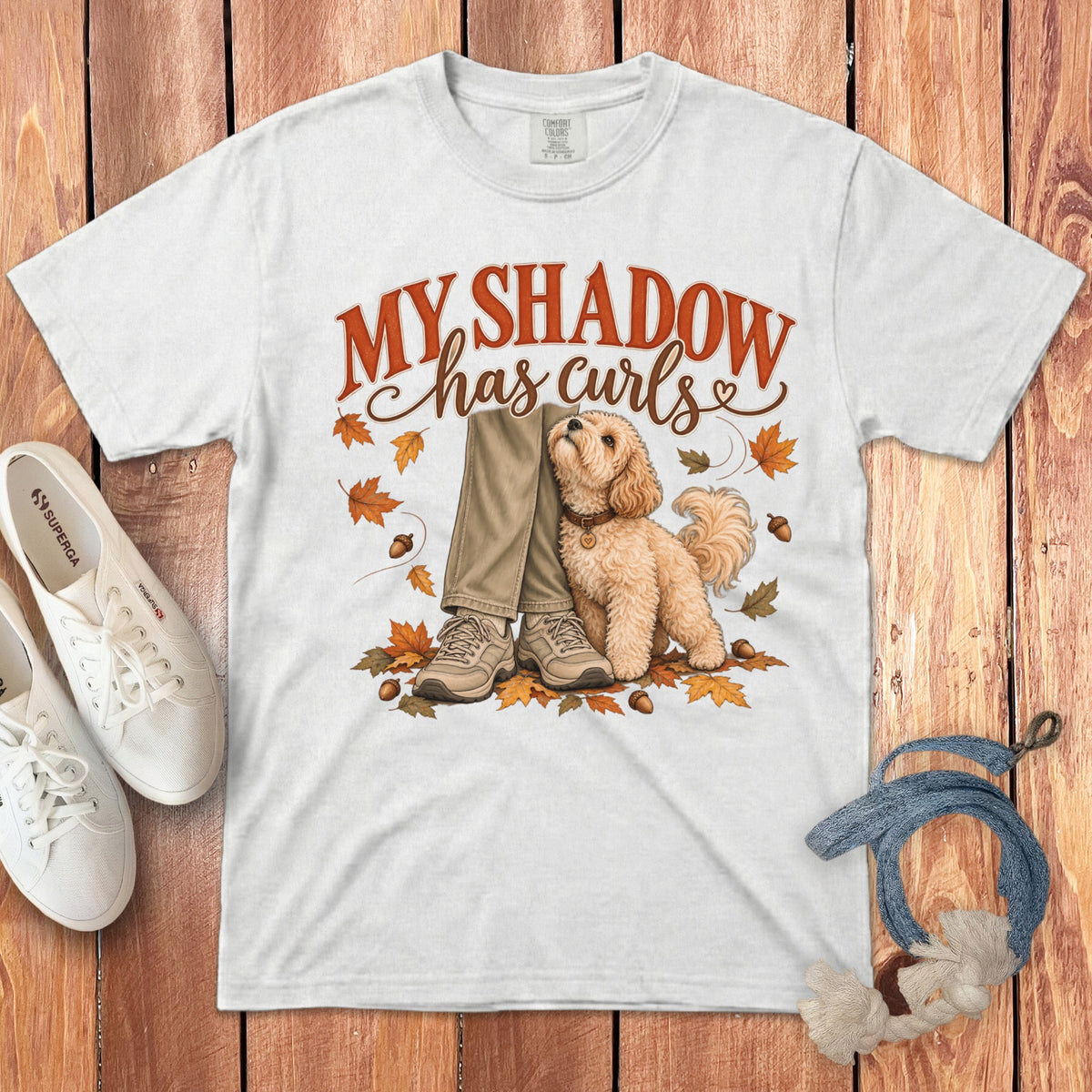 White t-shirt with a graphic of a fluffy dog sitting beside legs, surrounded by autumn leaves.