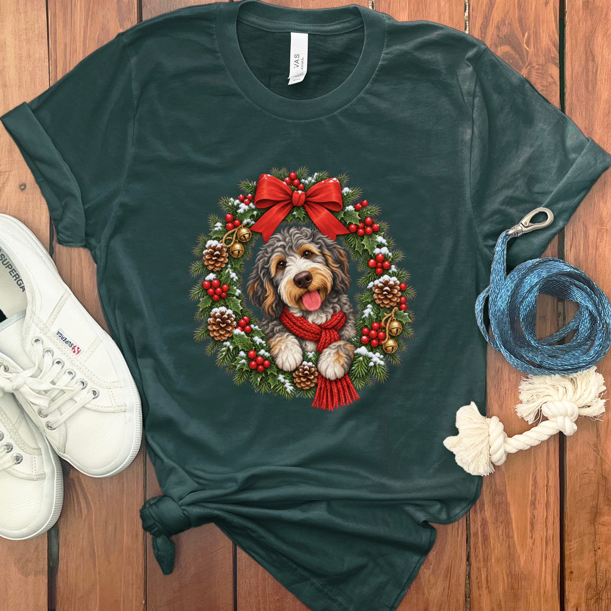 Dark green t-shirt featuring a doodle dog wearing a red scarf inside a Christmas wreath.