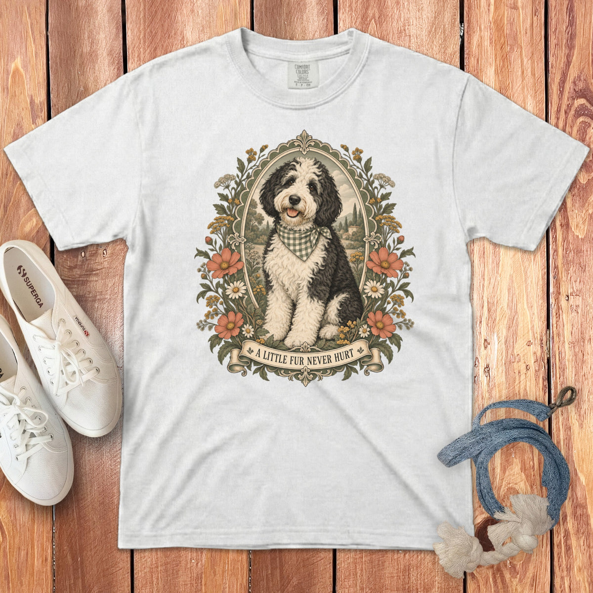 A white t-shirt featuring a framed graphic of a black and white doodle dog with flowers and the text A LITTLE FUR NEVER HURT.