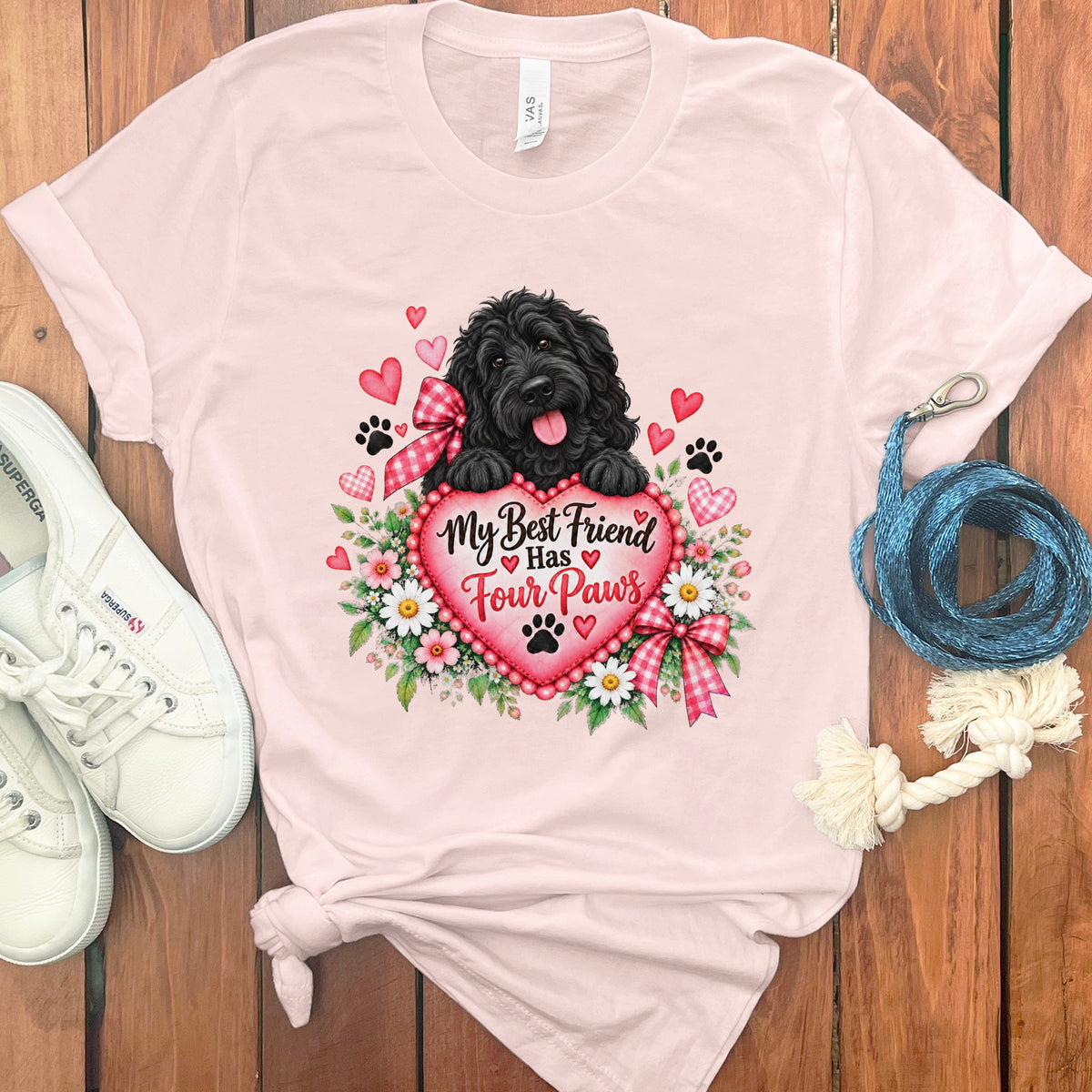 A light pink t-shirt features a graphic of a black dog holding a heart with text reading, My Best Friend Has Four Paws, surrounded by flowers and floating hearts.
