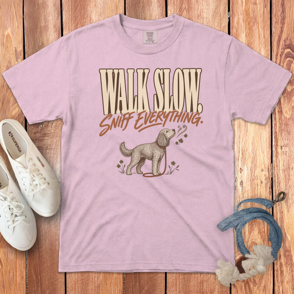 Pink t-shirt with the text Walk Slow Sniff Everything and a dog illustration, on a wooden background.