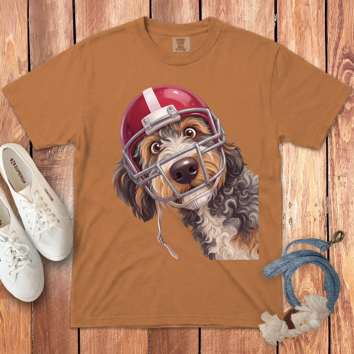 Dog wearing a red football helmet with a surprised expression on a brown t-shirt.