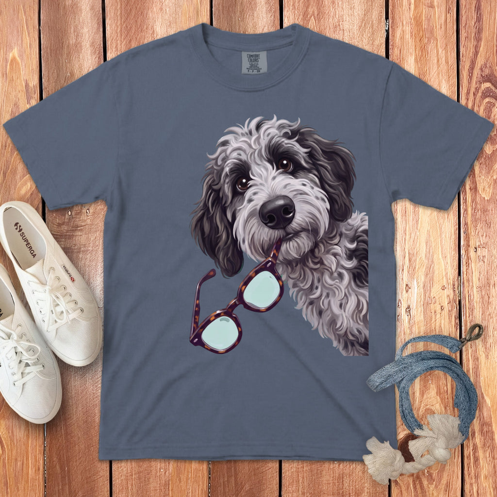 Slate blue t-shirt featuring a fluffy dog holding glasses in its mouth, laid on wood.
