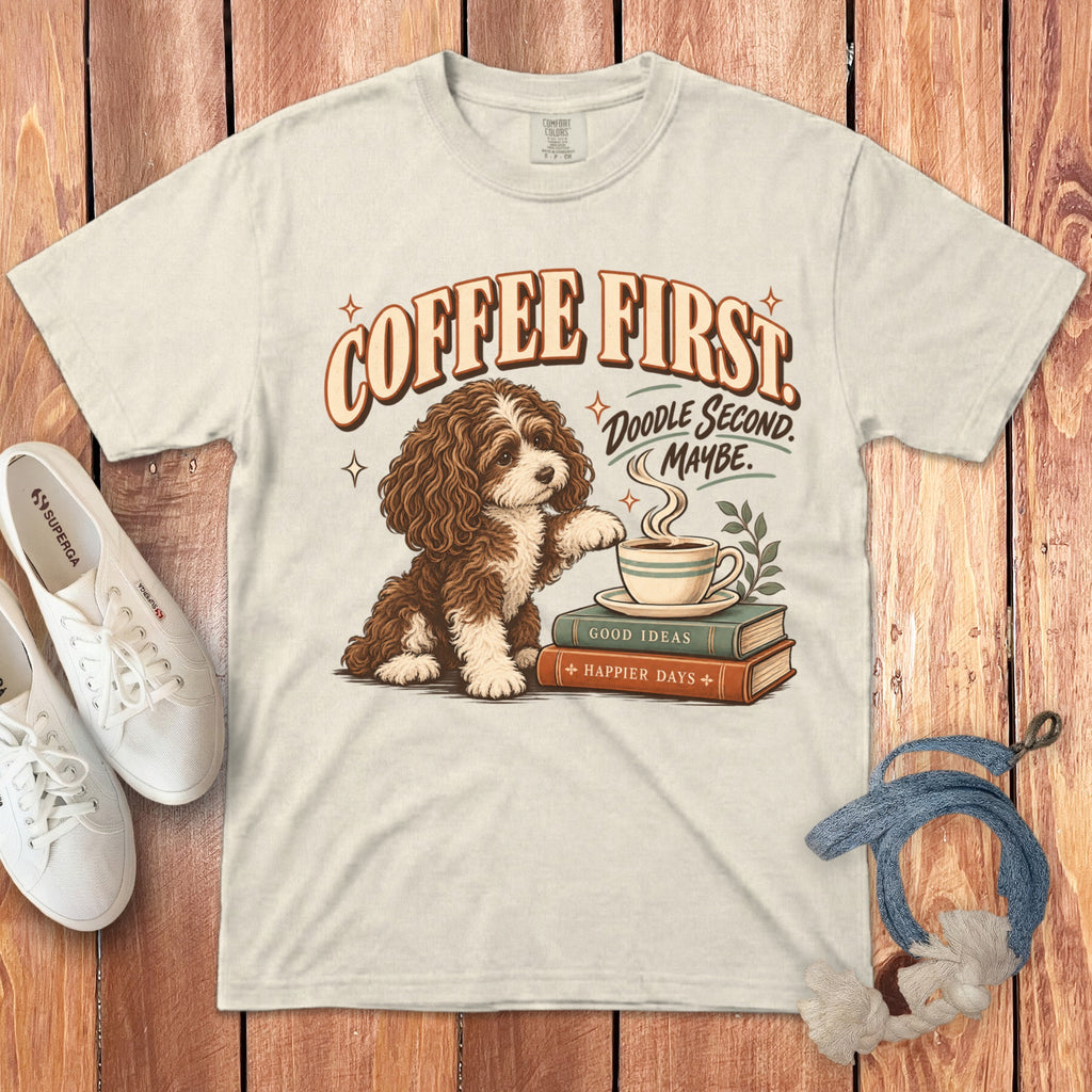 Off-white t-shirt featuring a graphic of a brown and white dog sitting near books and a coffee cup, surrounded by the text Coffee First Doodle Second Maybe.