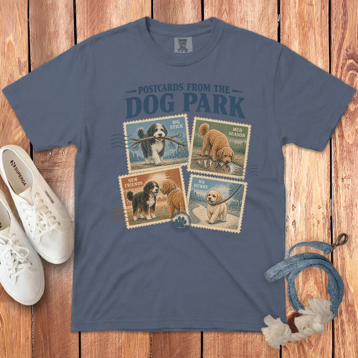 A blue t-shirt printed with Postcards from the Dog Park graphic design featuring four dog stamps.