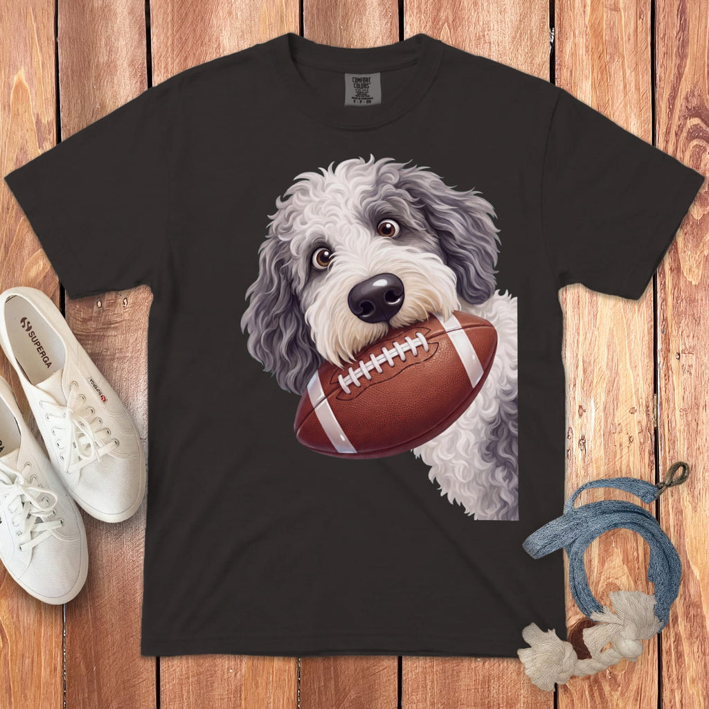 Gray and white doodle dog with a football in its mouth on a dark t-shirt.