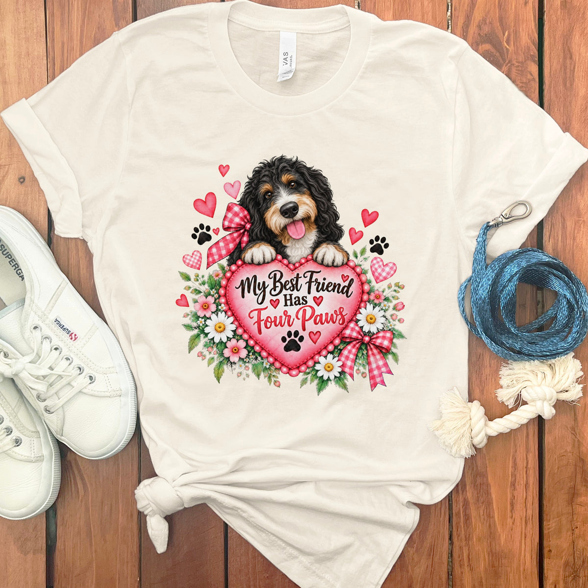 A cream t-shirt with a graphic of a Bernedoodle dog behind a large pink heart reading My Best Friend Has Four Paws, surrounded by flowers, hearts, and paw prints.