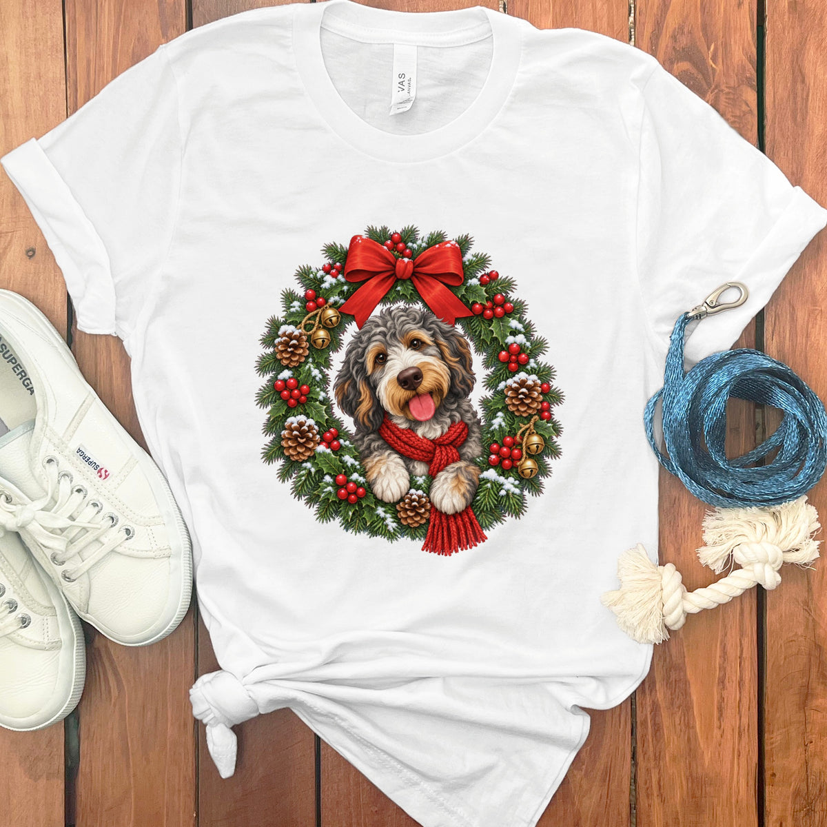 A white crewneck t-shirt featuring a graphic of a dog wearing a red scarf inside a Christmas wreath.