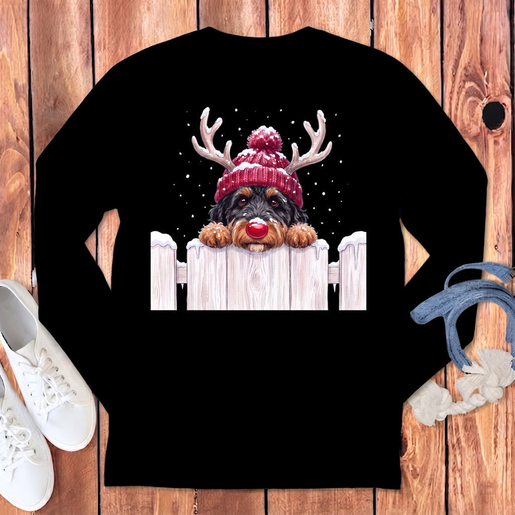 Dog with antlers and red nose peeking over a wooden fence with snow.