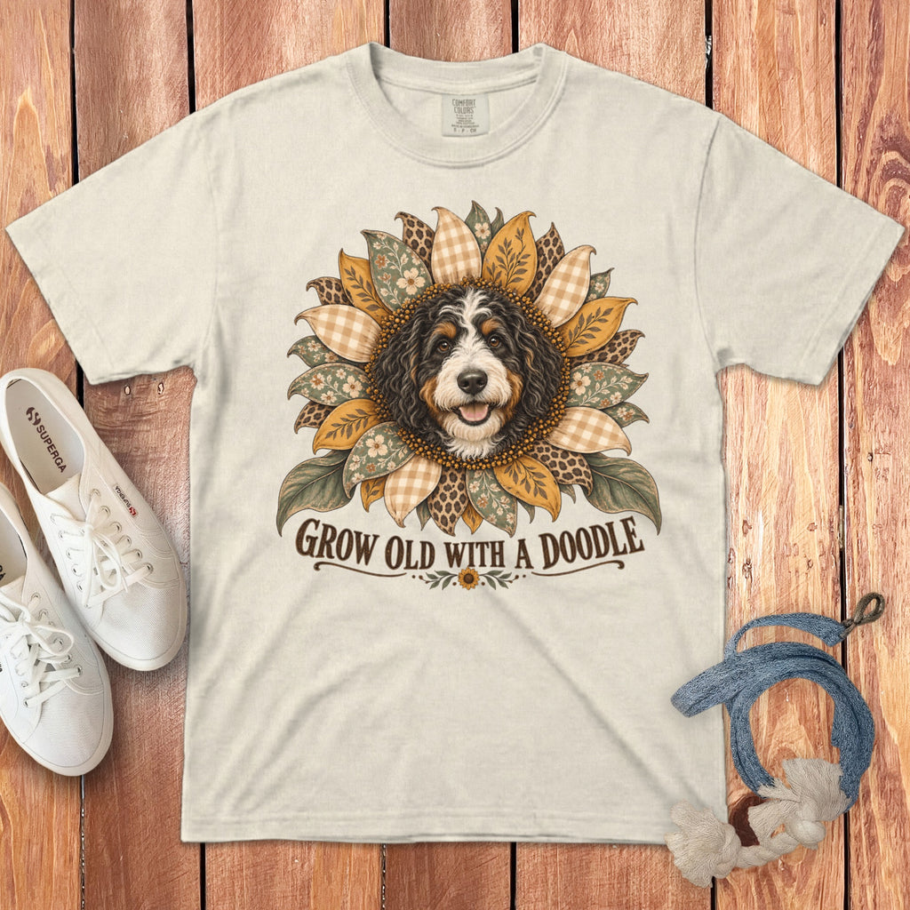 A cream t-shirt with a graphic of a Bernedoodle surrounded by patterned sunflower petals and the text Grow Old with a Doodle.