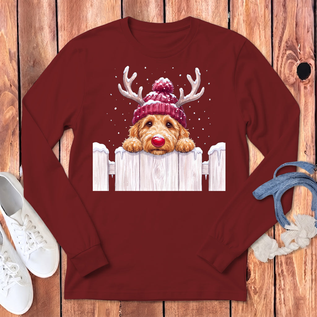Christmas doodle dog with antlers and red hat peeking over snowy fence.