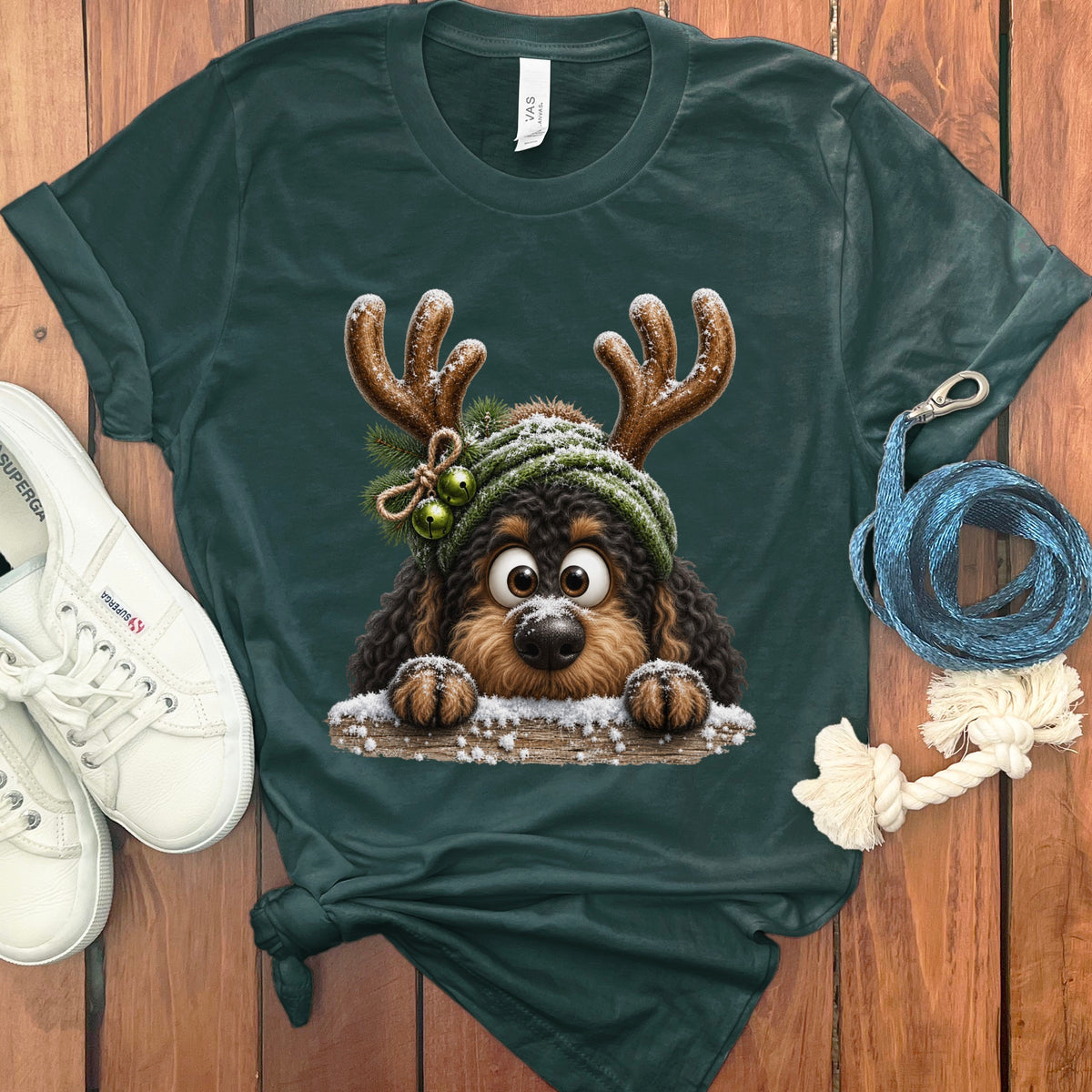 Dog with antlers and green hat peeking over a snowy log, on a dark green shirt.
