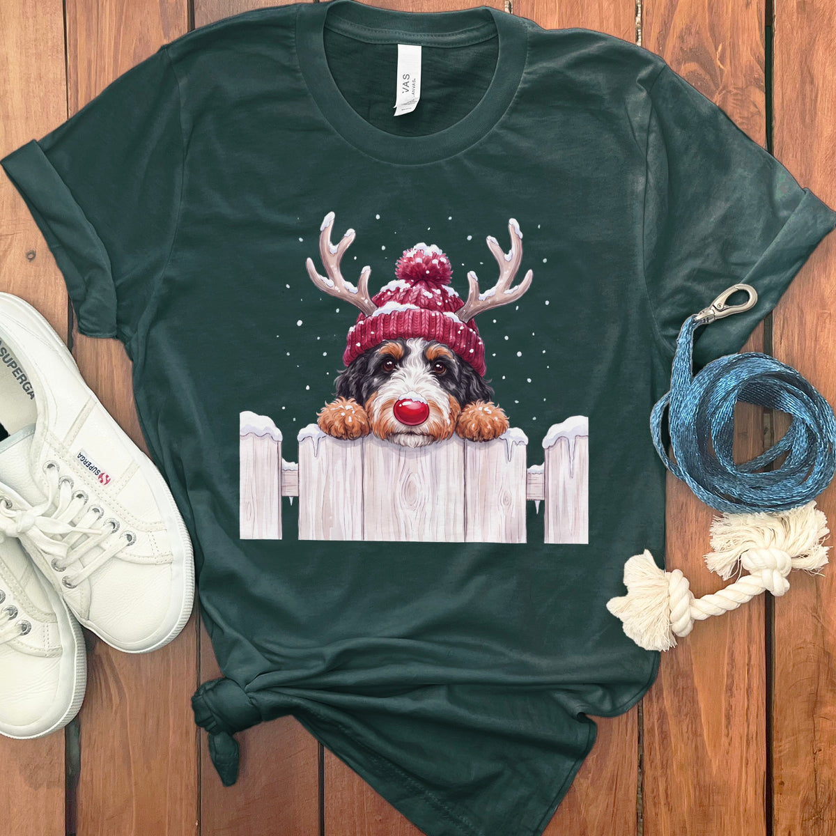 Bernese mountain dog wearing reindeer antlers and red hat peeking over a fence.
