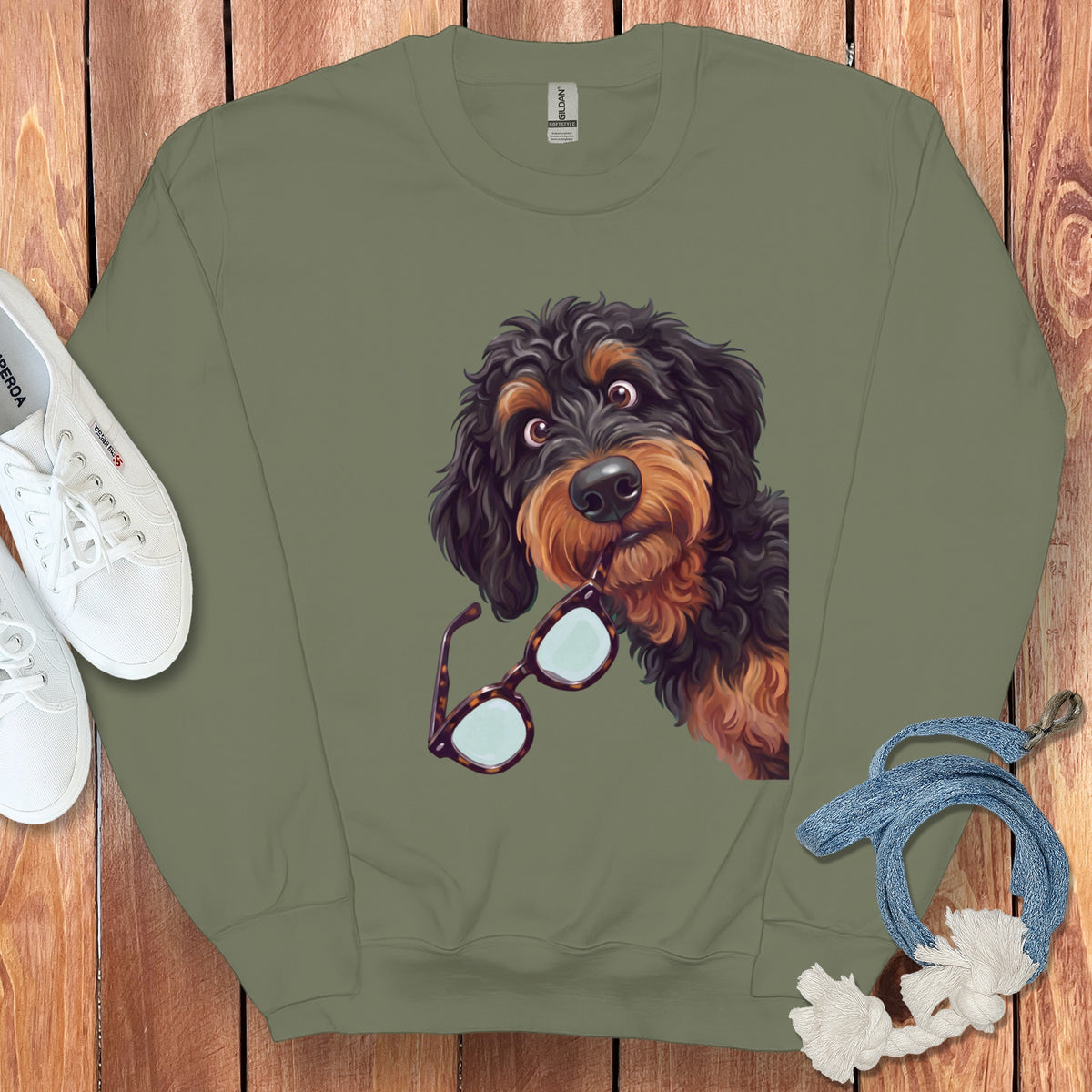 An olive green crewneck sweatshirt featuring an illustrated black and brown dog holding glasses in its mouth.