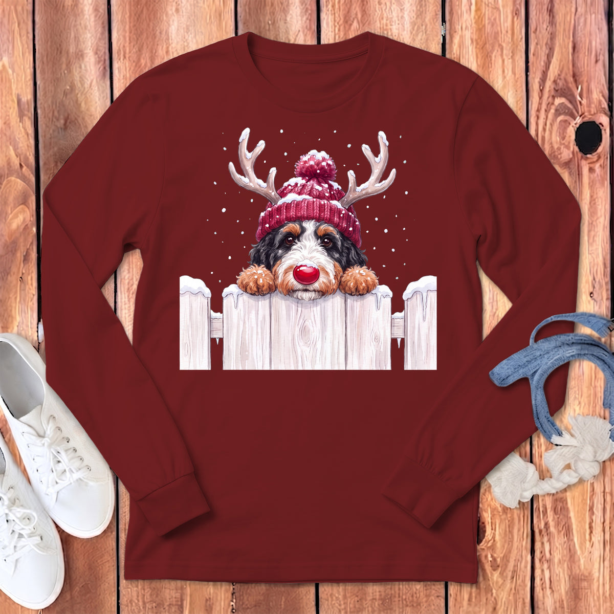 Bernese Mountain Dog wearing reindeer antlers and red hat peeking over fence.