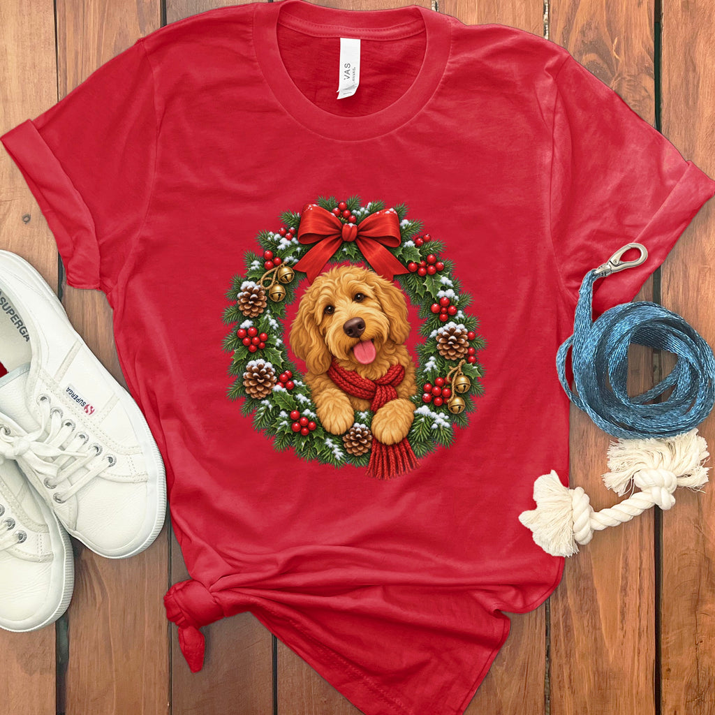 Flat-lay of a red t-shirt with a Golden Retriever wearing a red scarf inside a Christmas wreath graphic.