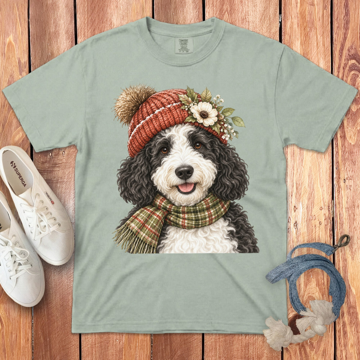 Light green t-shirt with watercolor illustration of a dog wearing a winter hat and scarf.