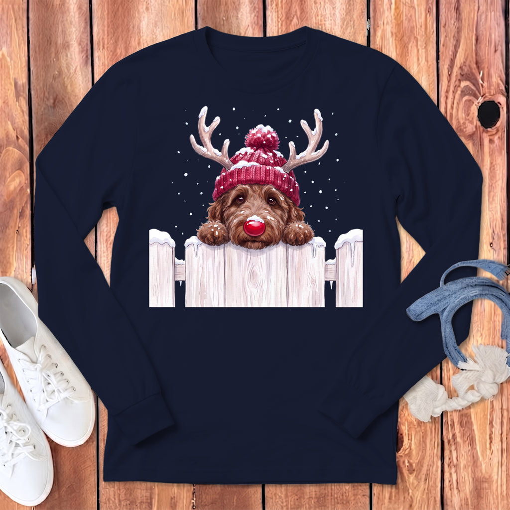 Brown dog wearing a red beanie with antlers and a red nose peeks over a snowy fence.