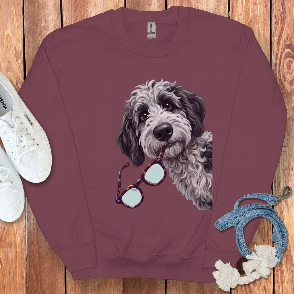 Maroon crewneck sweatshirt featuring a graphic of a fluffy doodle dog holding tortoiseshell glasses in its mouth.