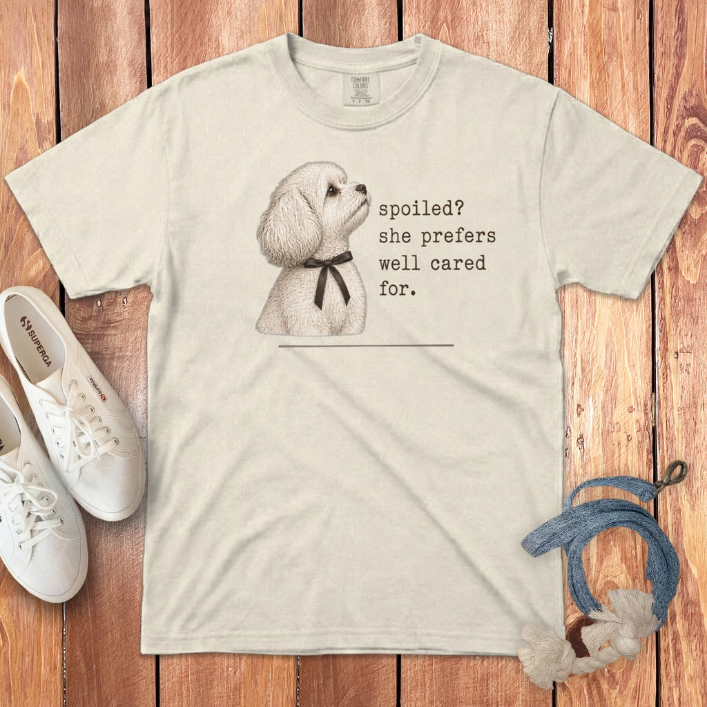 A cream-colored t-shirt featuring a poodle graphic with the text spoiled she prefers well cared for.