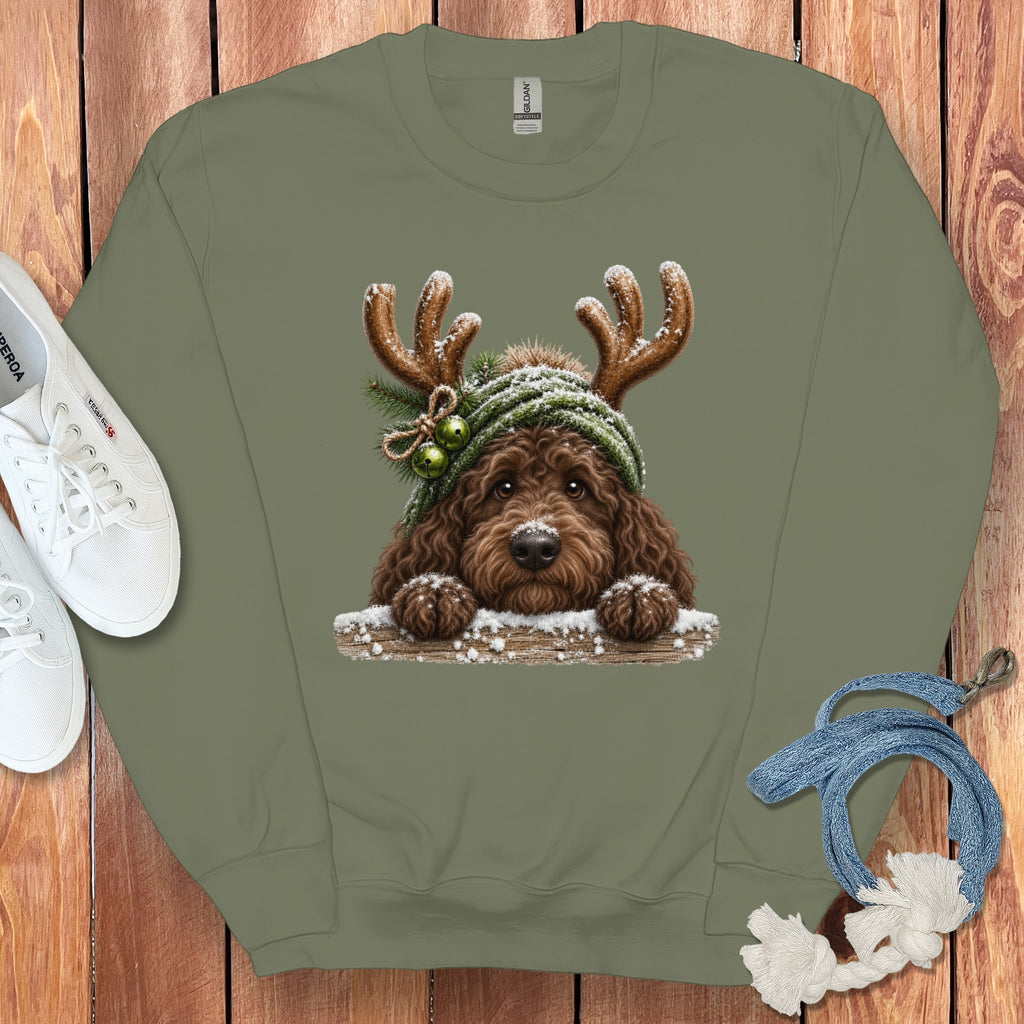Brown dog with antlers and a green hat, peeking over a snowy log.