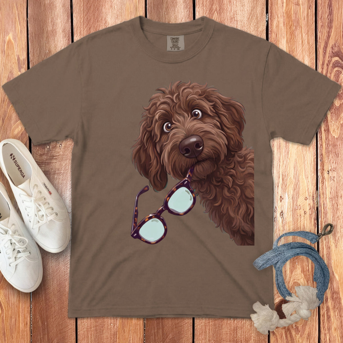 Brown t-shirt featuring an illustration of a brown doodle dog holding tortoiseshell glasses in its mouth.