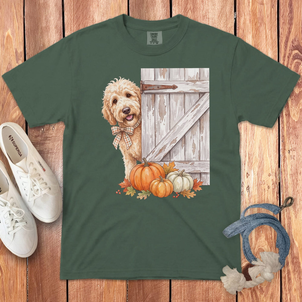 Green t-shirt featuring a golden doodle peeking from behind a rustic wooden door with pumpkins.