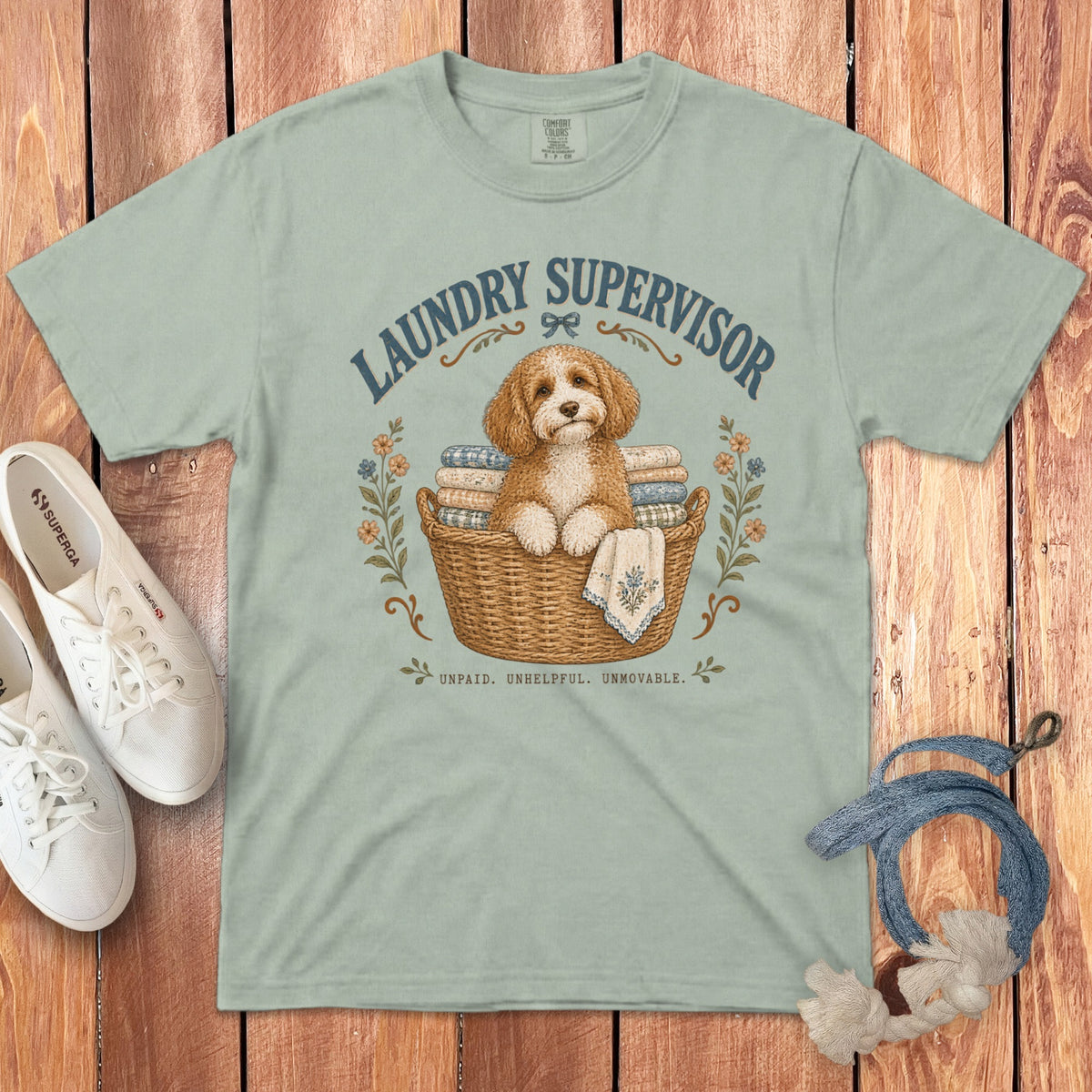 Sage green t-shirt with a graphic of a curly puppy in a laundry basket and text that reads Laundry Supervisor.