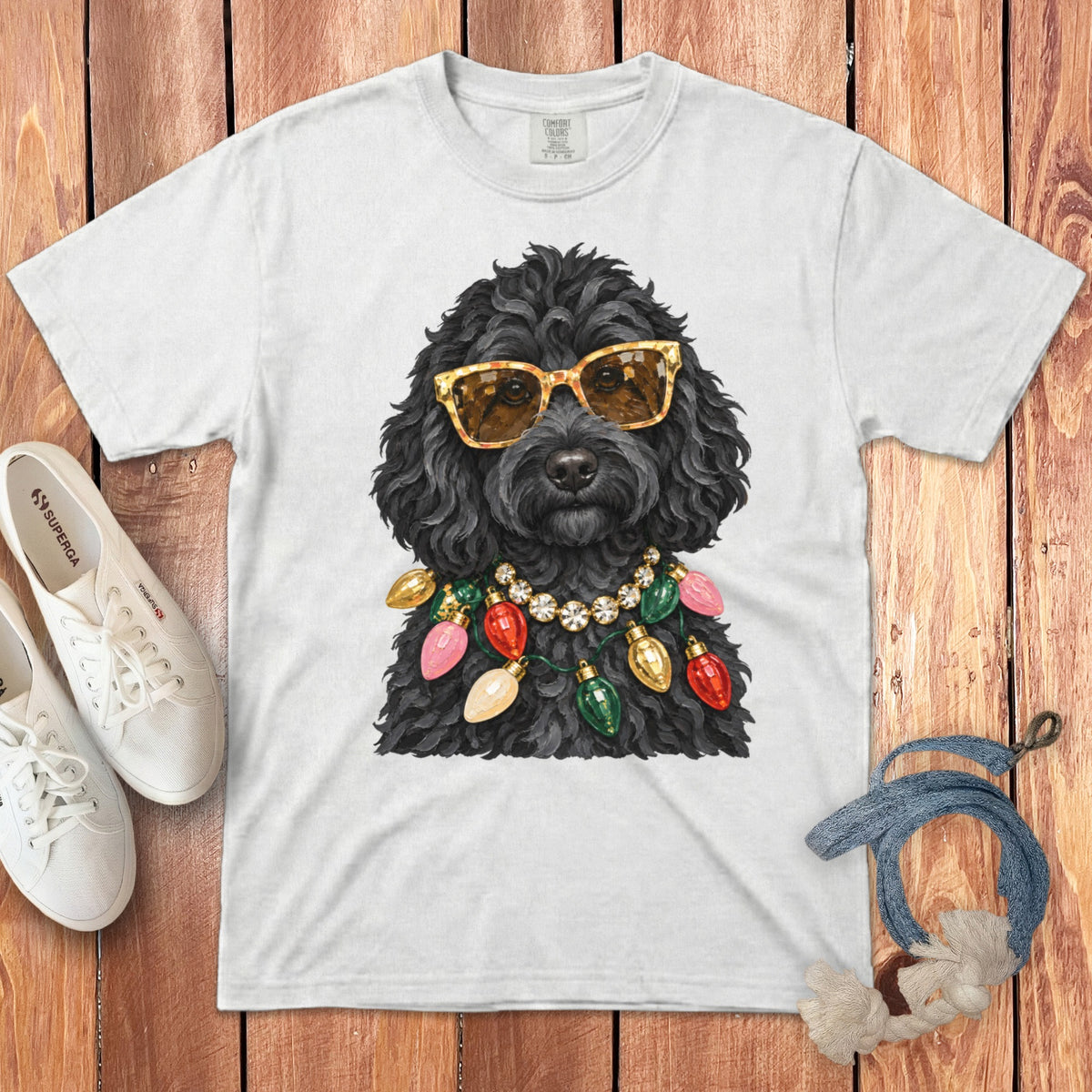 Black poodle wearing sunglasses and a Christmas light necklace on a white t-shirt.