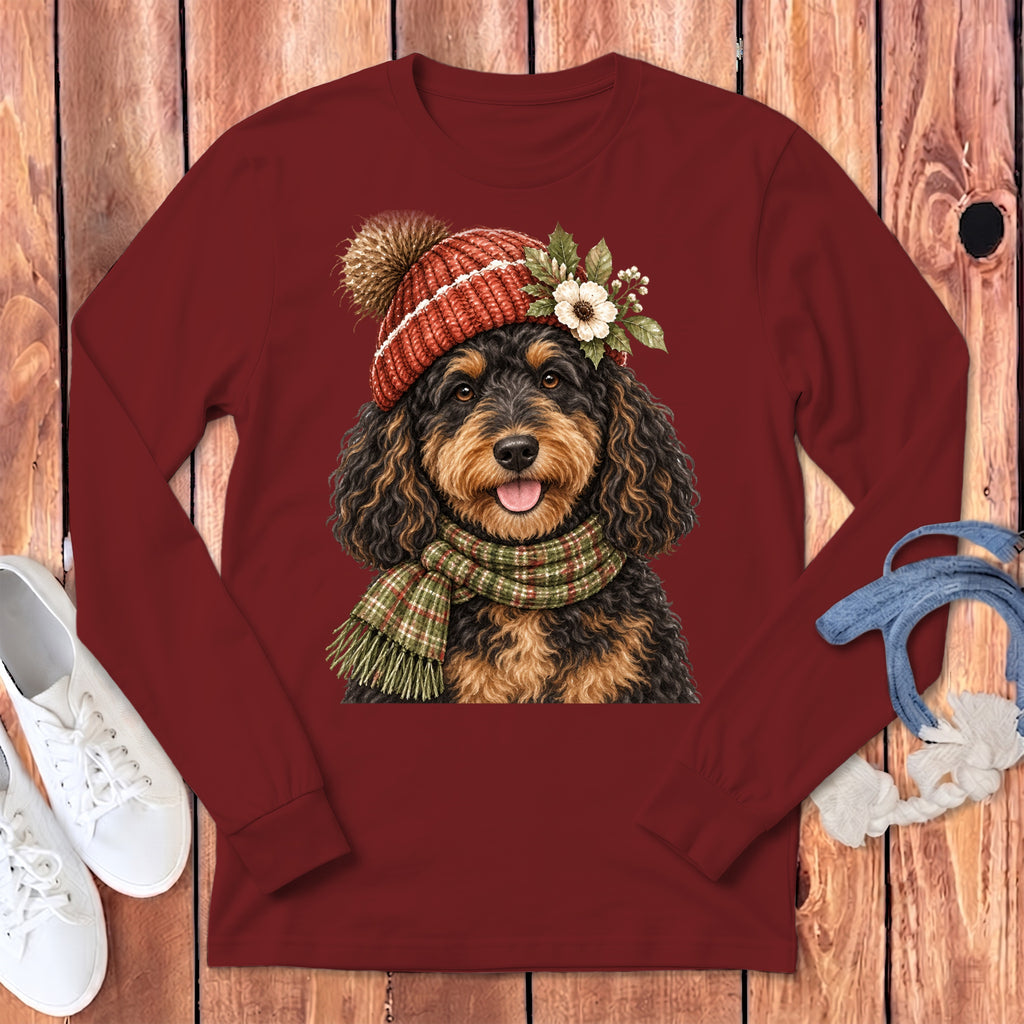 Fluffy dog in festive hat and scarf on maroon long sleeve shirt.