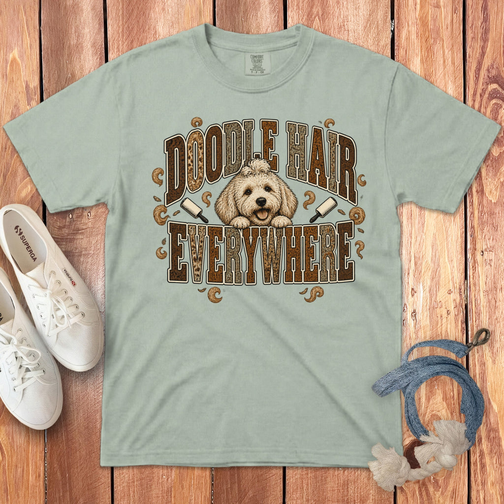 A light green t-shirt with a Doodle Hair Everywhere graphic, flanked by white shoes and a leash on a wooden background.