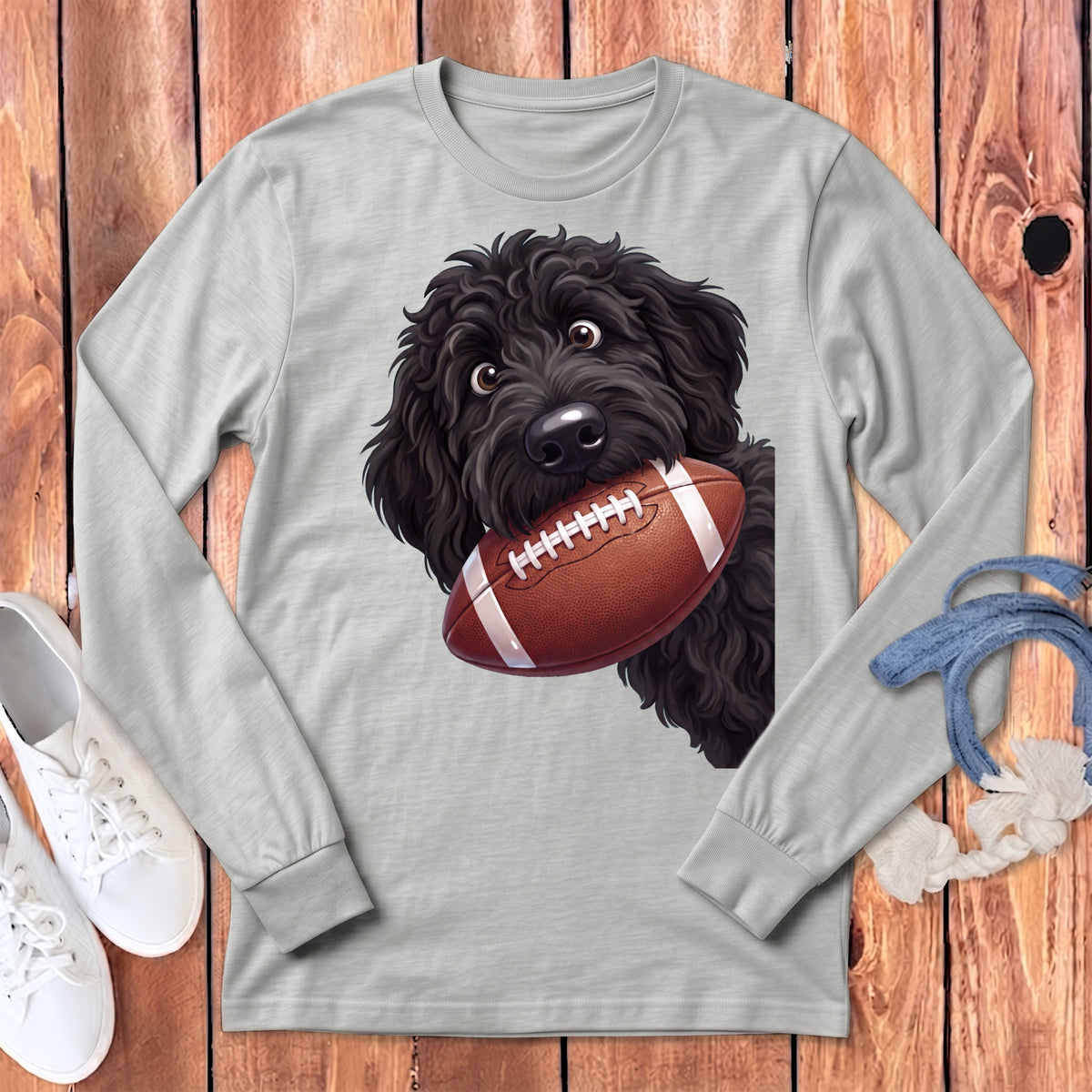 Black shaggy dog holding a football on a light gray long-sleeve shirt.