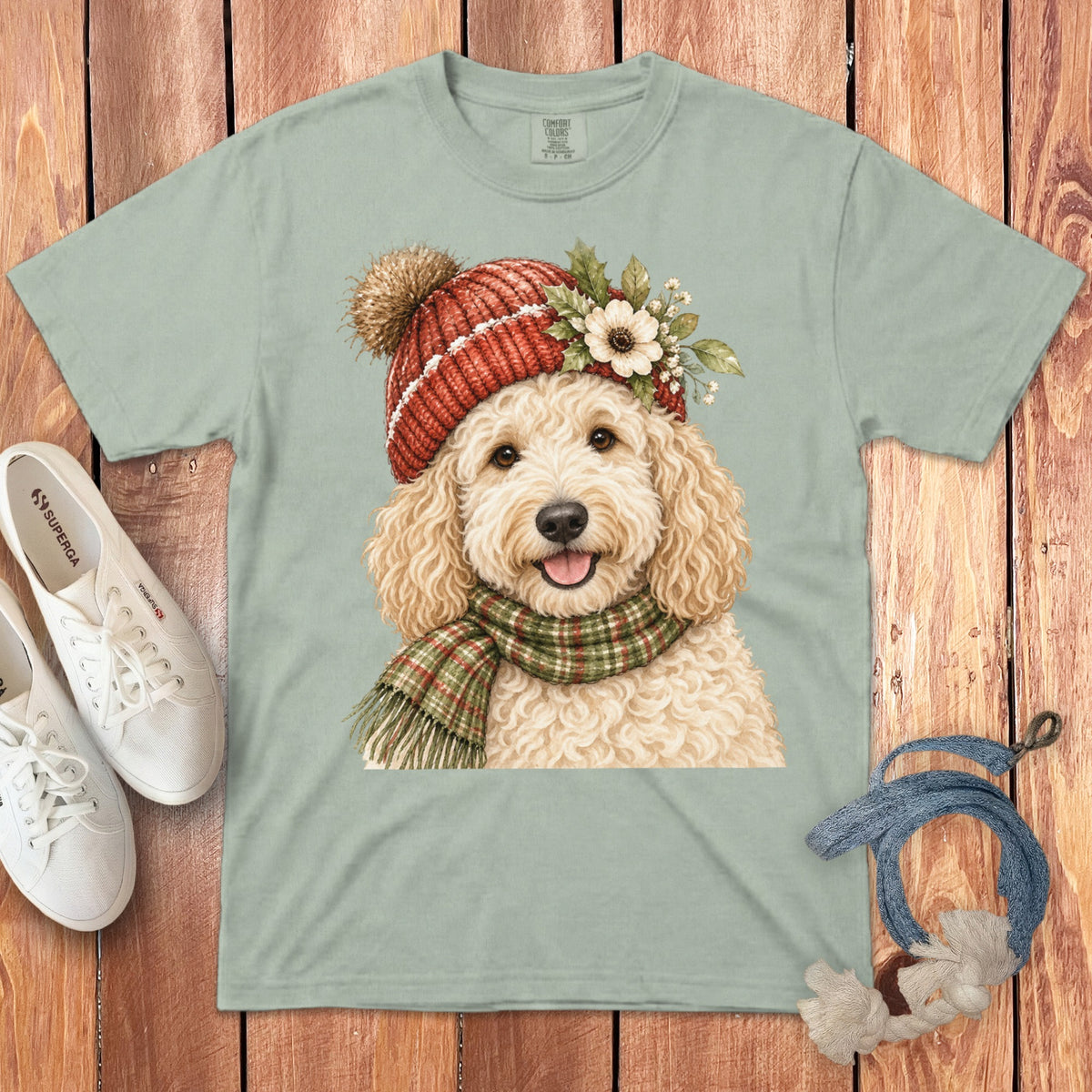 Light green t-shirt with a drawing of a fluffy dog wearing a red knit hat and plaid scarf.
