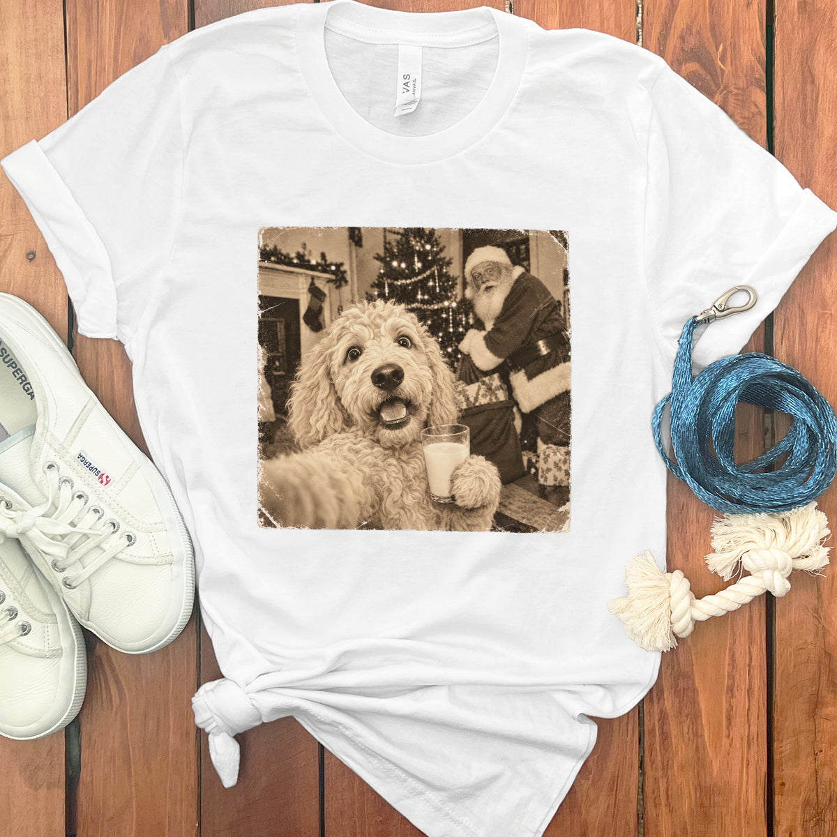 A white t-shirt featuring a sepia-toned graphic of a fluffy dog taking a selfie with Santa Claus.
