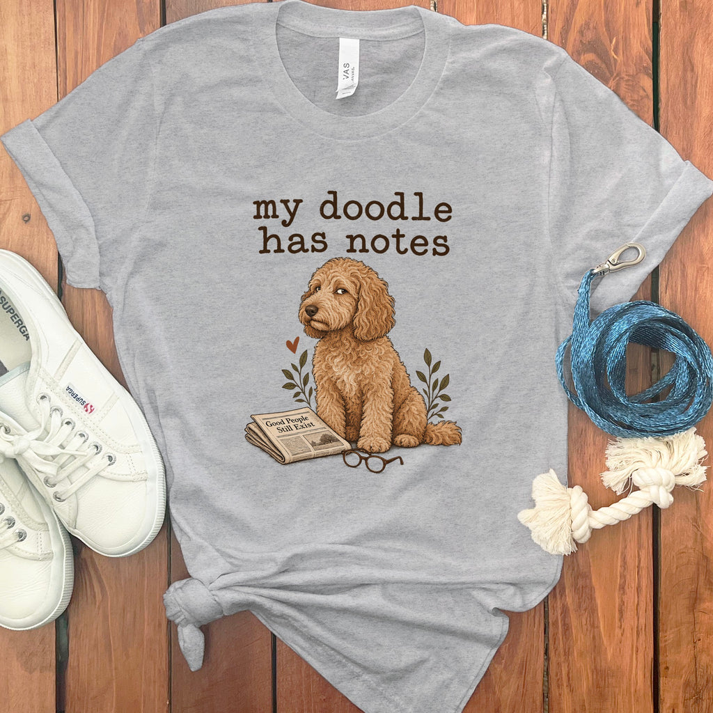Gray t-shirt with a doodle reading a newspaper titled "Good People Still Exist".