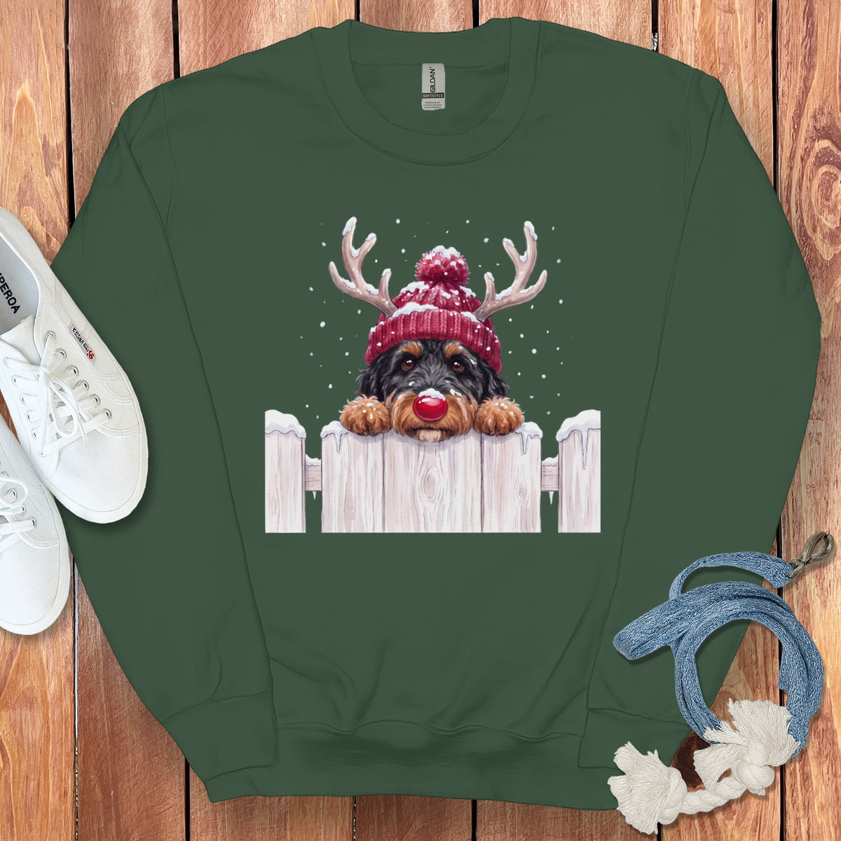 Green sweatshirt with a dog wearing a Santa hat and antlers, peeking over a fence.