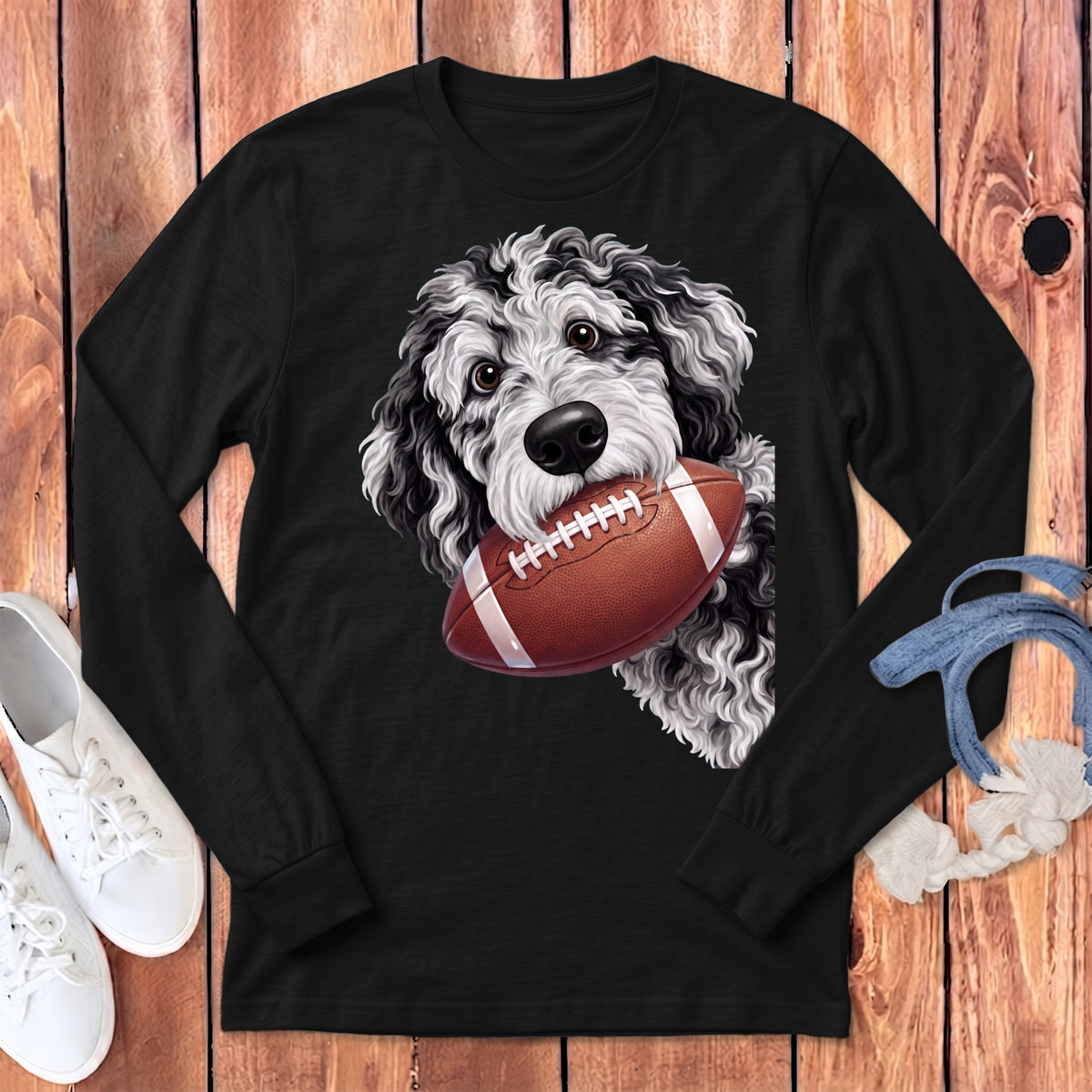 A black long-sleeve shirt featuring a fluffy black and white dog holding a football in its mouth.