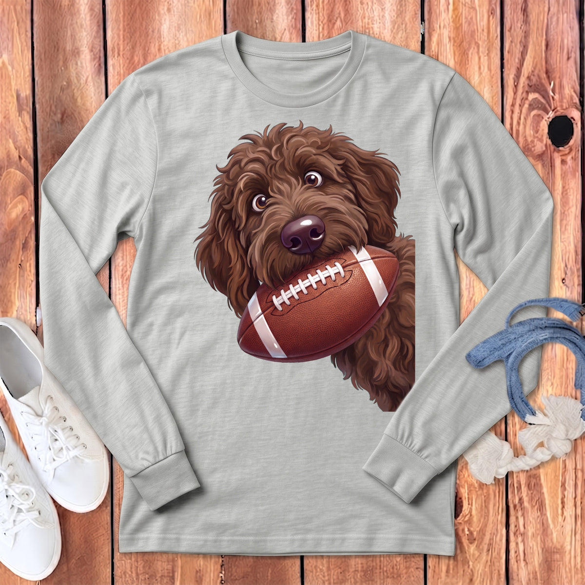 Brown doodle dog with a football in its mouth on a grey long-sleeve shirt.