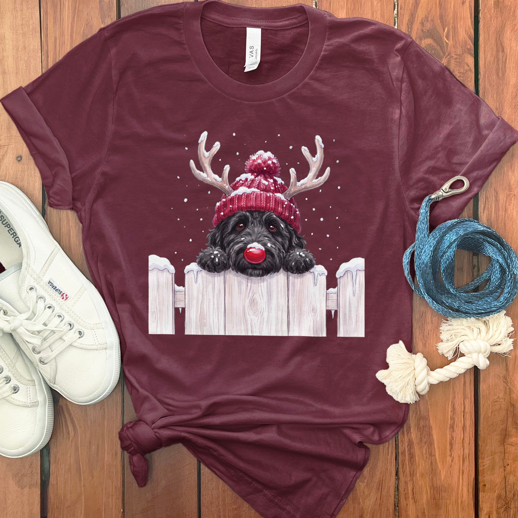 Maroon t-shirt with a black dog wearing a Santa hat and reindeer antlers over a white fence.